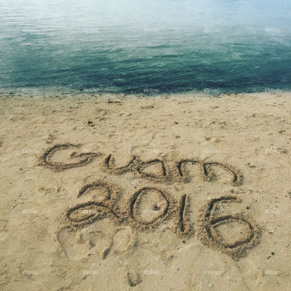 Guam 2016 written in the sand in front of the ocean 