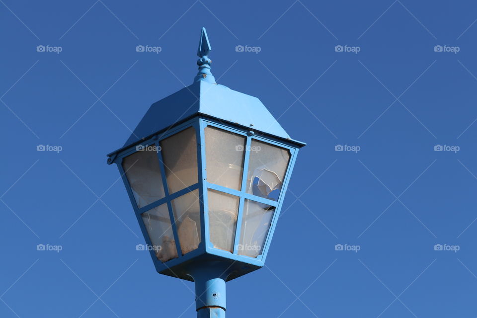 Minimalism: vintage blue streetlamp with broken glass inserts against a vivid clear blue sky