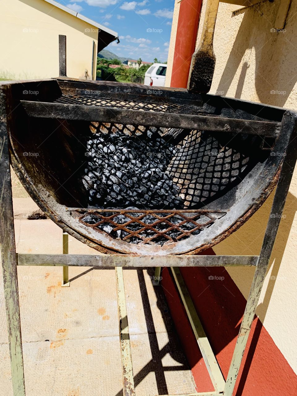 A burned metal braai stand with a mesh net, burned charcoal and ashes after a meat braai.