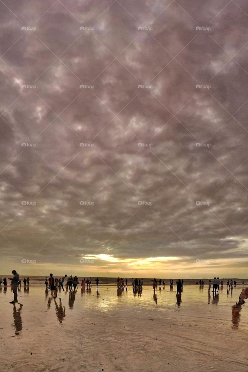 blend of yellow purple grey coloured clouds and the shinny beach surface.A pretty Sunset photo of Juhu beach, Mumbai.