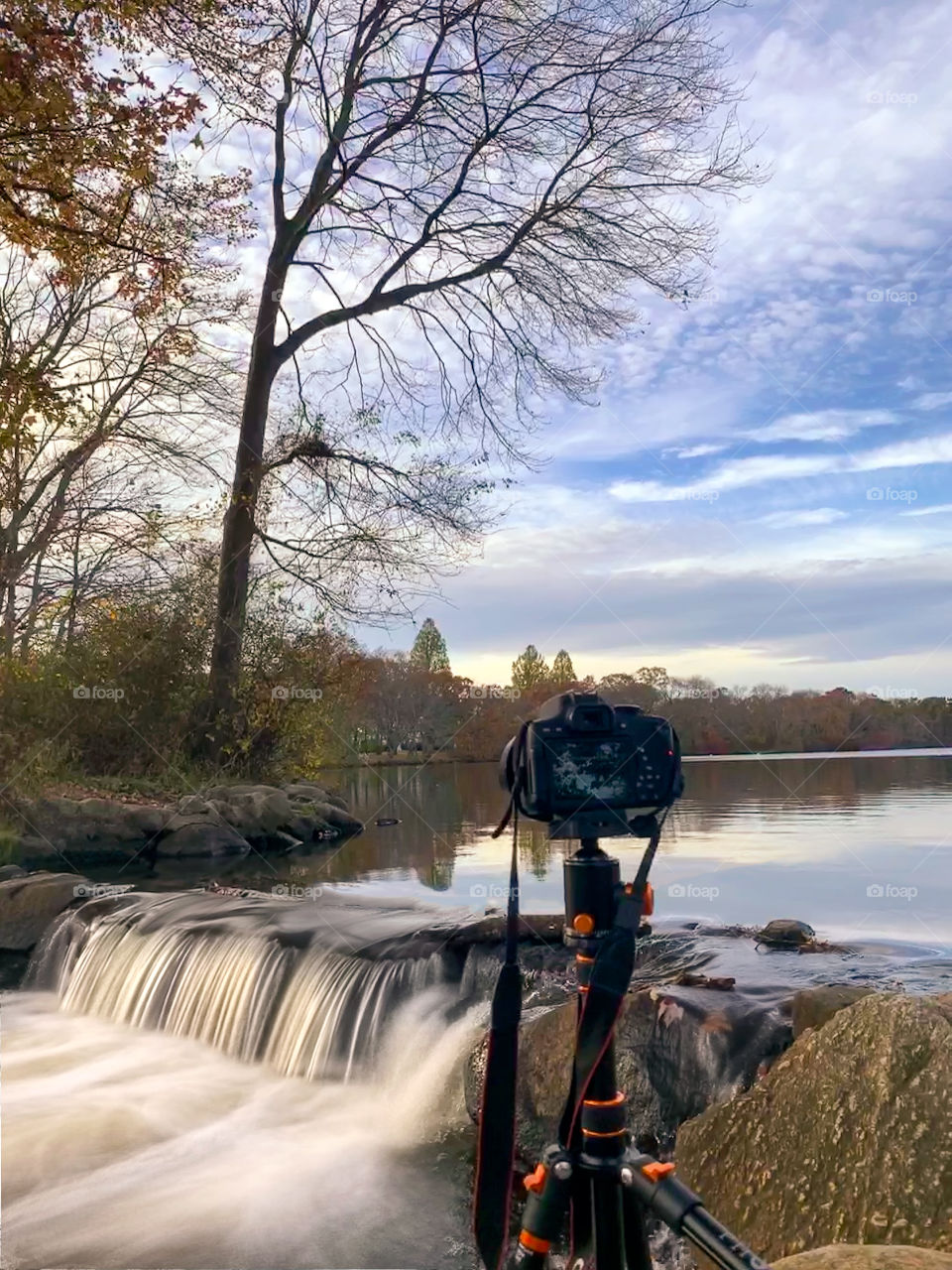 Long exposure photo of a DSLR camera on a tripod, taking a photo on a small waterfall trickling down from a peaceful nature scene. iPhone 10