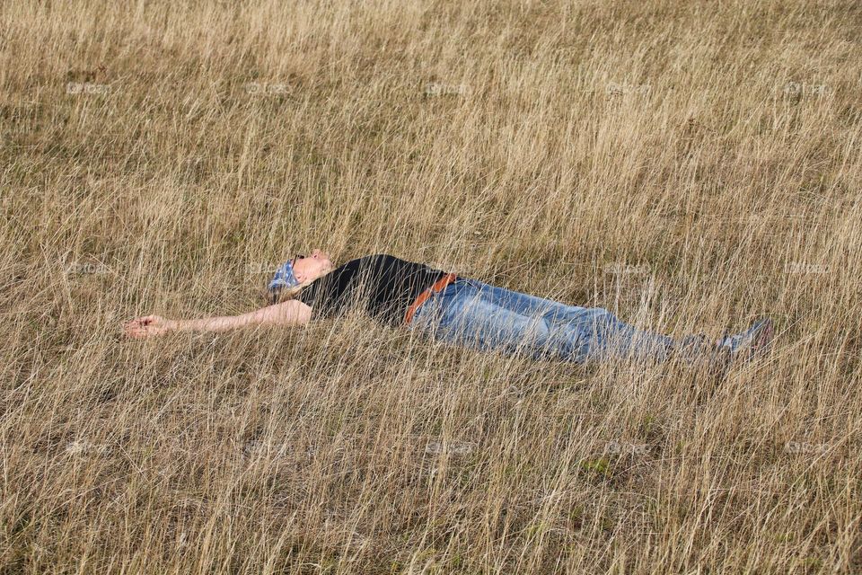 A woman lies relaxed with her arms outstretched in a dry brown meadow and sleeps