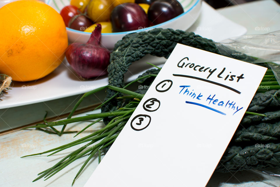 Grocery list - think healthy on wood table with superfoods in background, citrus, orange, greens, kale fruits and vegetables 
