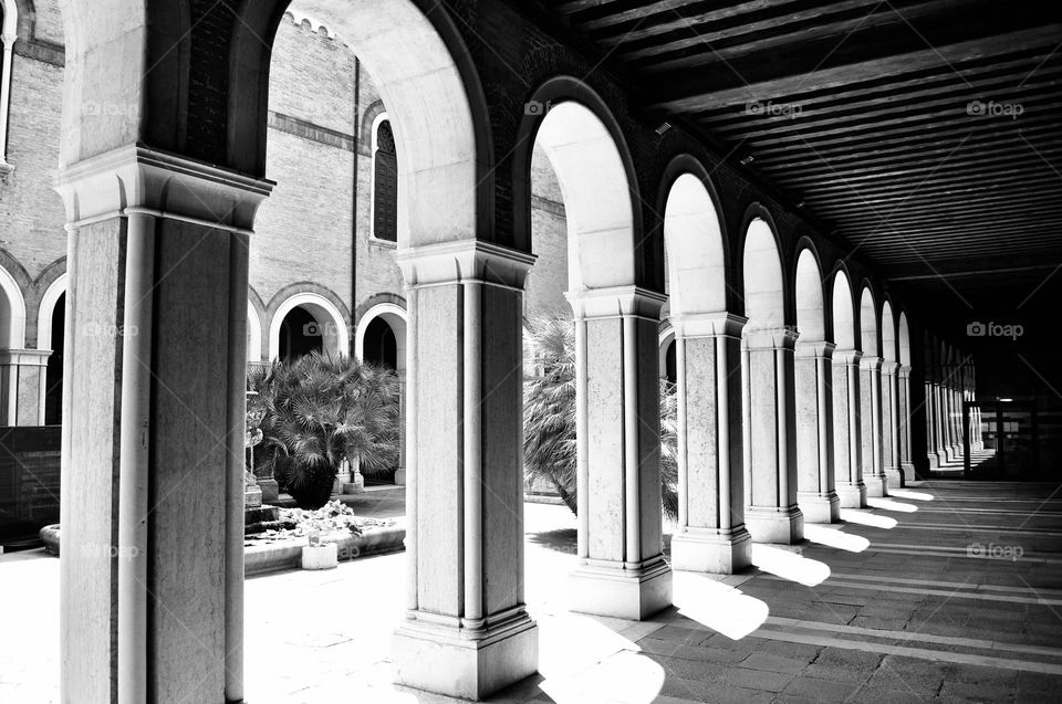 Portico composed of a series of arches through which sunlight filters, play of light and shadow in architecture, Venetian palace