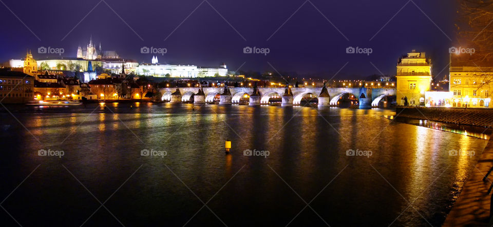 View from the island on an architectural monument of Charles bridge overlooking the Vysehrad. Long glimpses of night lights and architectural lighting in the broad waters of the Vltava River