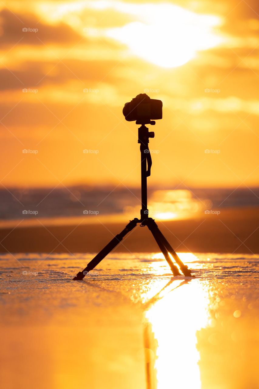 A DSLR camera set up on a tripod capturing a beautiful sunset on a beach.