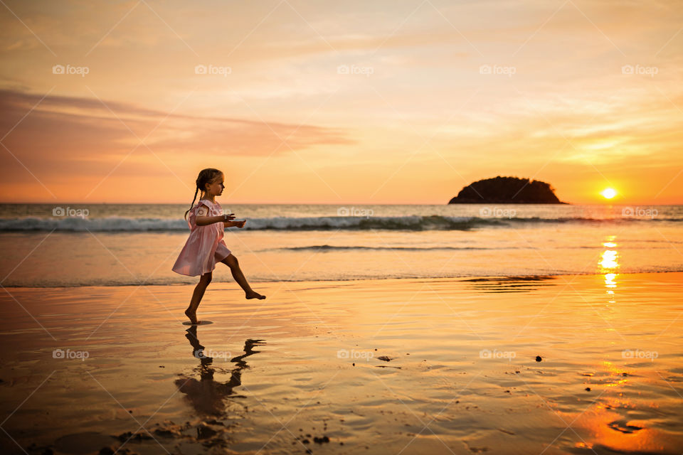 Little girl with blonde hair walking on the sandy beach on sunset 