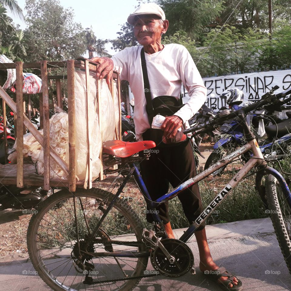 An old man is enjoying his work.  He sells crackers by riding a bicycle.  Photo taken on October 13, 2019.