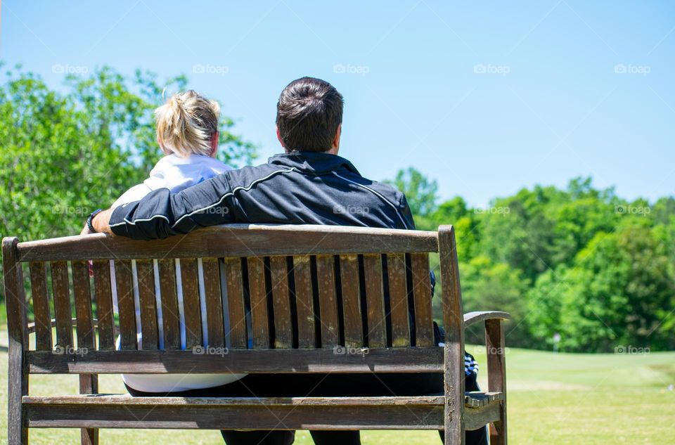 A couple sitting on the bench on a golf course in nature 