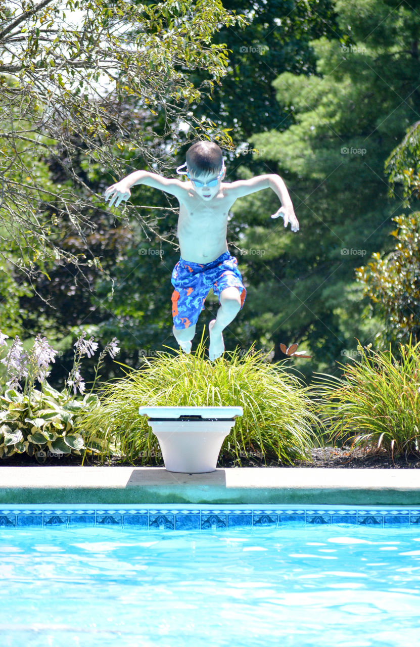 Young boy jumping off of a diving board into a pool