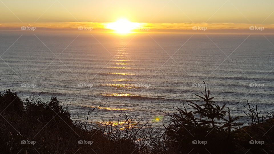View of golden sunset over ocean from bluff with golden clouds and reflection on surf