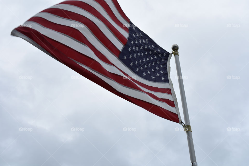 united states of American flag waving in the wind against cloudy grey gray sky