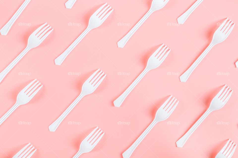 A lot of white plastic forks lying diagonally on a pink background, flat lay close-up. Cutlery and ecology concept.