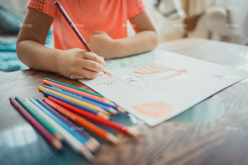 Little girl drawing with colorful pencils at wooden desk indoor