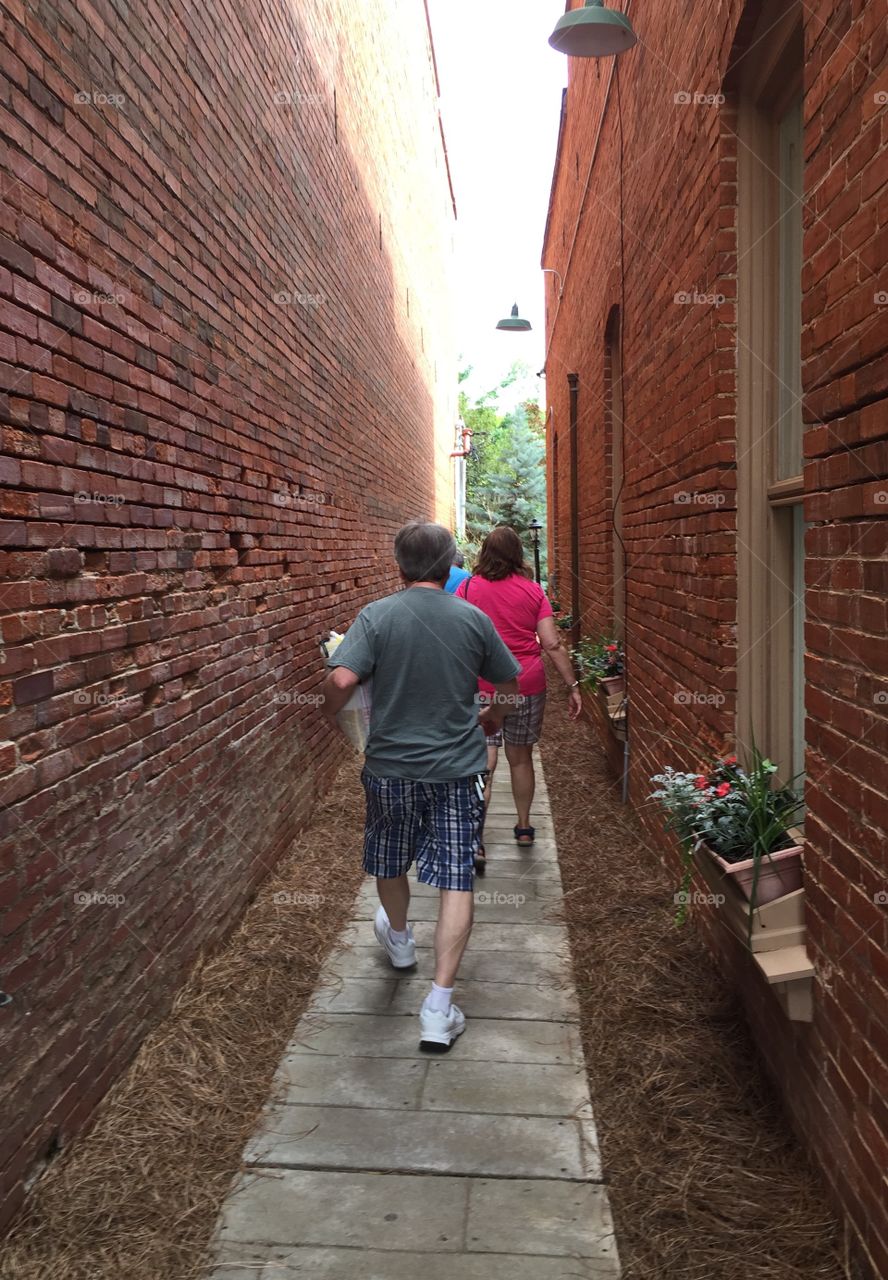 Back of couple seen walking down a narrow alleyway between two old building walls. 