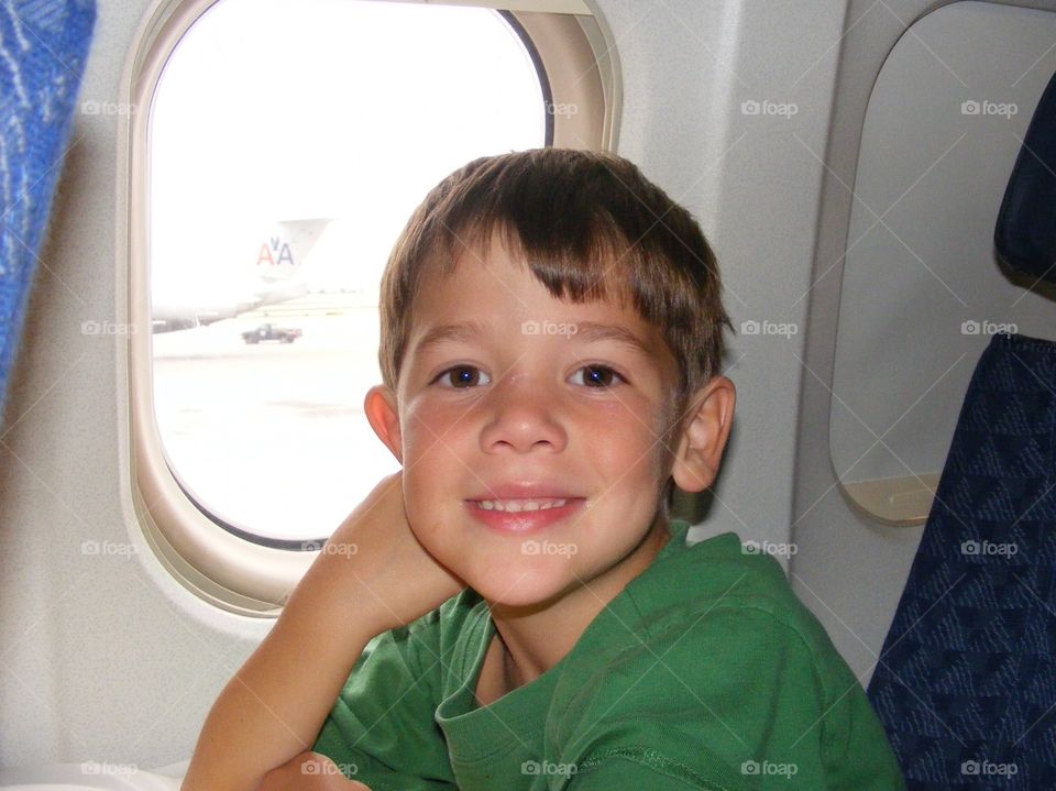 A boy sitting in the window seat of an airplane.