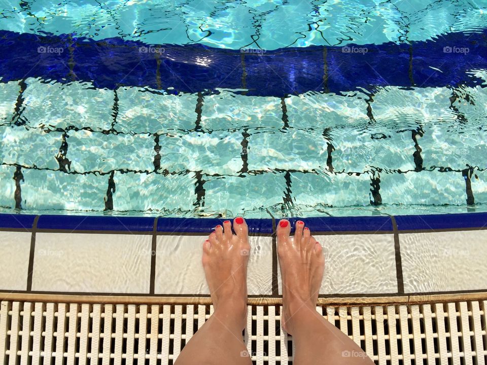 Woman's feet with red nails by the pool ready to get into the water