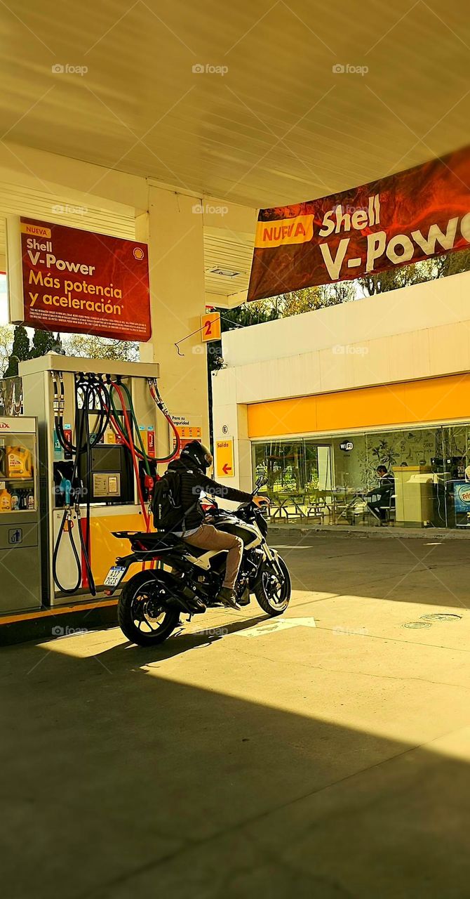 Motorcyclists at the pump stops to fuel up as he begins his day. His bike will take him more km than a car on a liter of fuel.