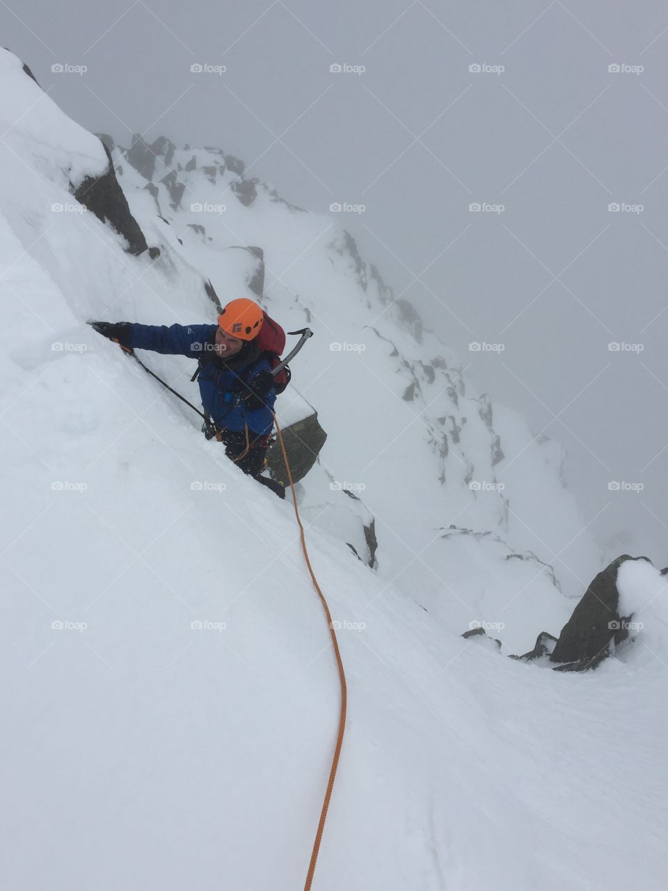 Male mountain climber going up snowy slope with rope