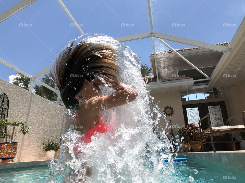 Giant water splash from kid jumping out of the pool  making a hair a water wave on a sunny day. 