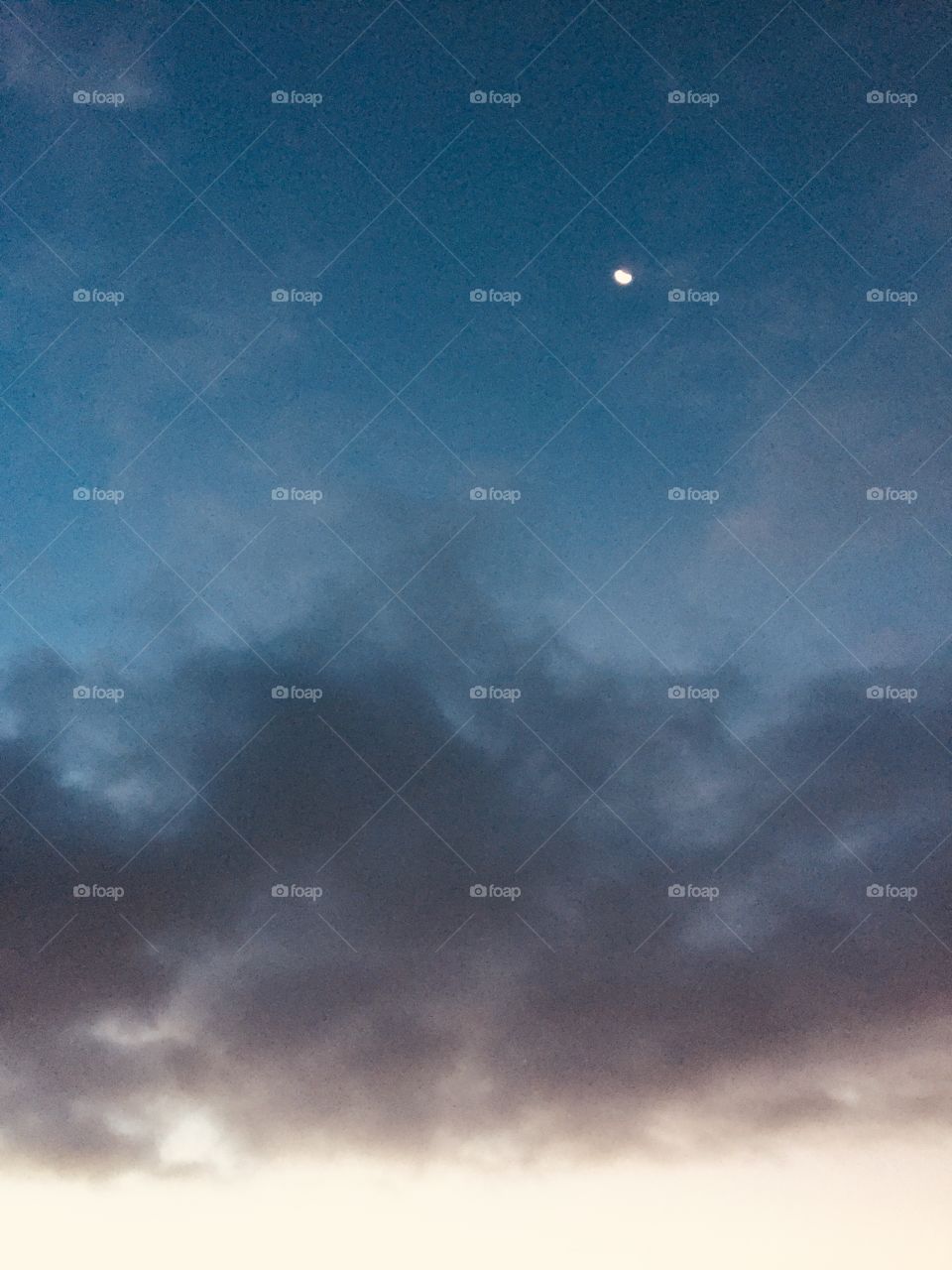 A gibbous moon, barely visible over layers of clouds in muted colors, being illuminated from beneath 