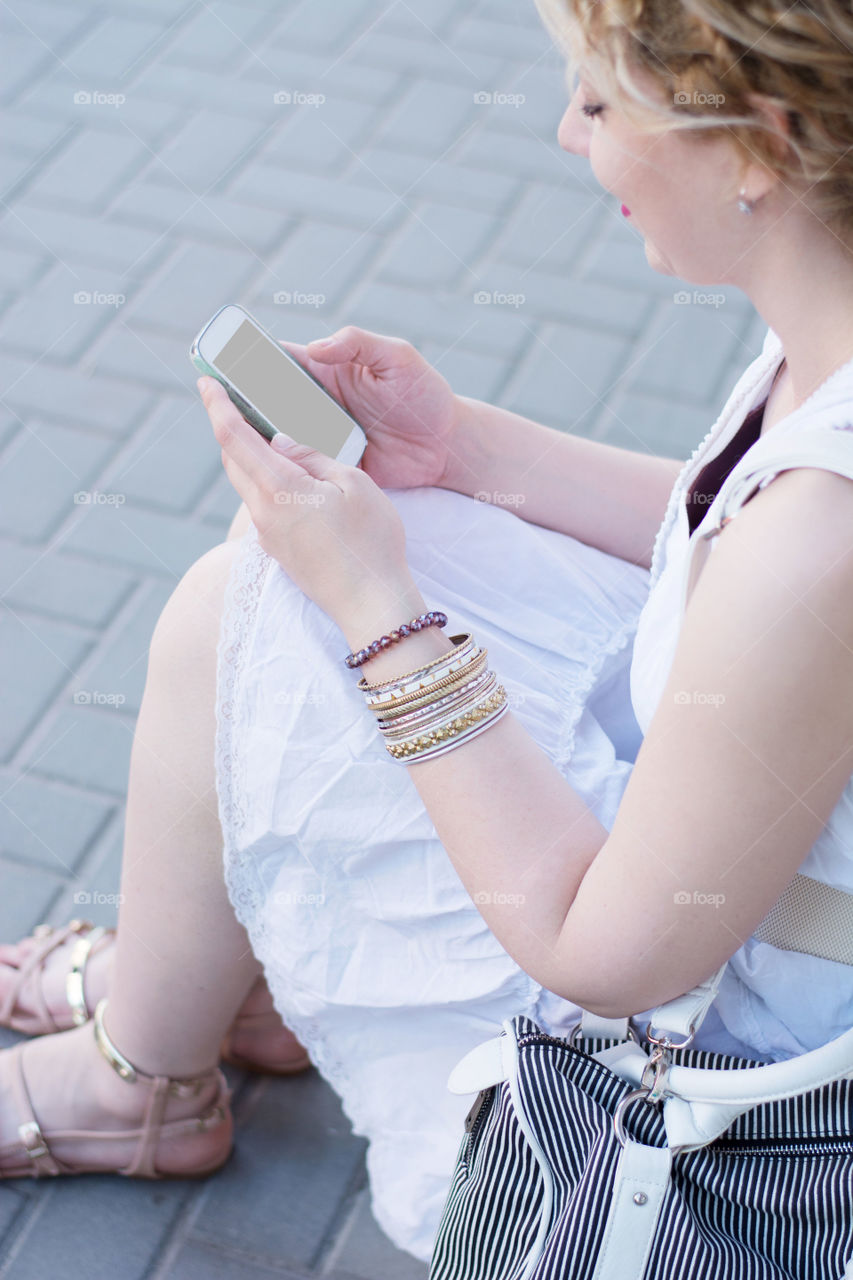 girl on the phone. curly blond girl using phone while sitting on the street 