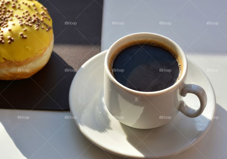 cup of coffee and bun sweet in sunlight on a white and brown background, morning routine