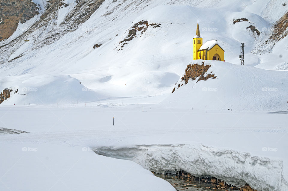 Small alpine church on a rock immersed in the snow