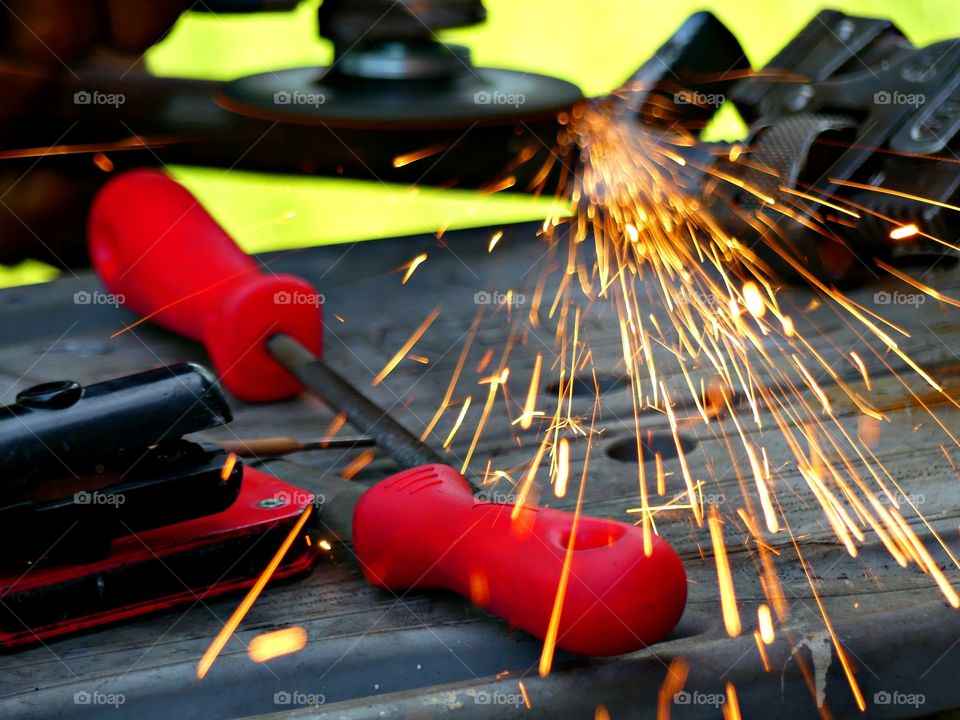 Color Red:  Sparks flying as a man works on a welding project using red handled tools