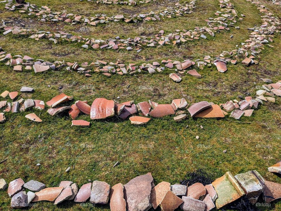 Pottery shards in a circular pattern on the grass, rings within rings of broken clay pieces