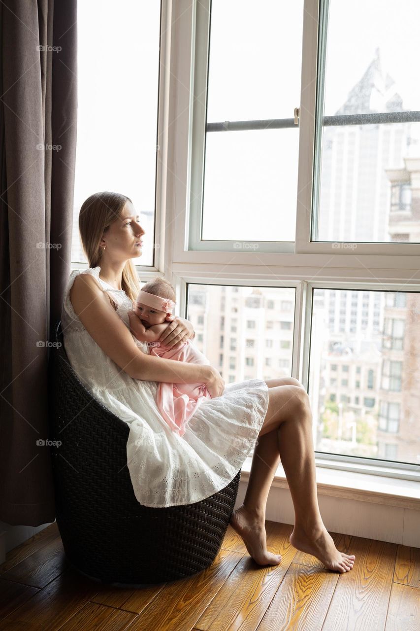 Young Caucasian mother hugging her newborn daughter near window 