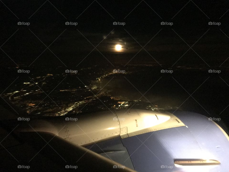 Aerial shot of Moon behind clouds over city lights