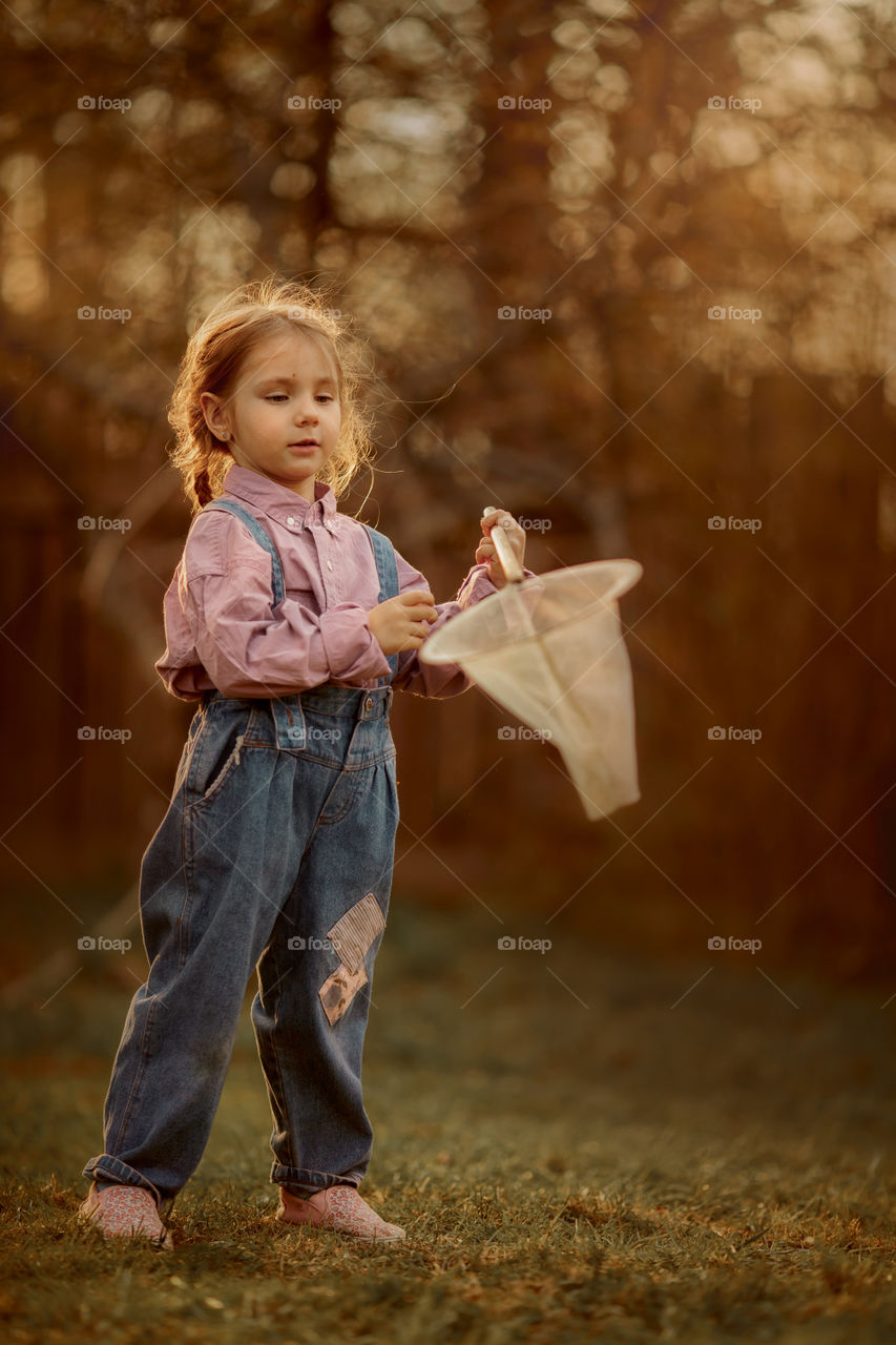 Little girl with butterfly net outdoor at sunset