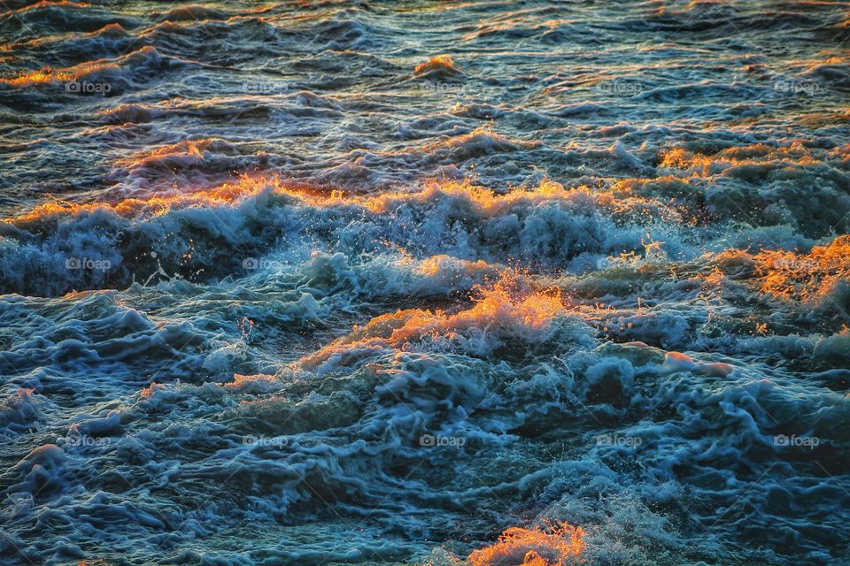 sea ​​waves at sunset spray and foam illuminated by the orange evening sun