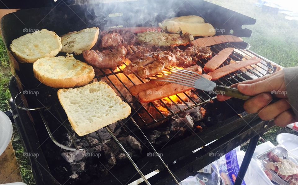 Human hand preparing sausages on grill