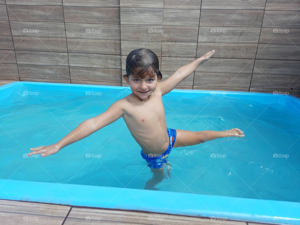 blond boy with blue eye smiling in blue swimming pool.