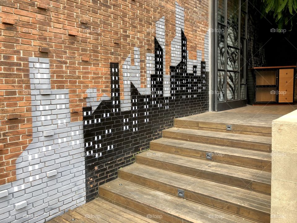 Red brick wall cityscape mural 1. Wood steps and open doorway. Taken August 2018.