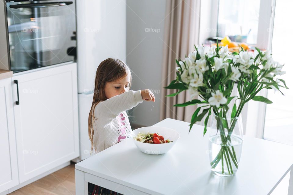 Bouquet of flowers in vase on table at home, little girl on kitchen 