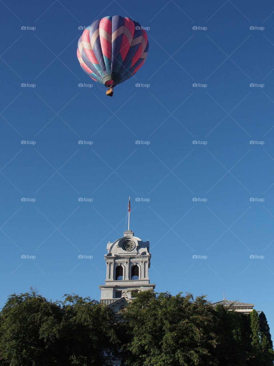 A colorful hot air balloon flies over the historical Crook County Courthouse in Prineville in Central Oregon on a sunny summer morning. 
