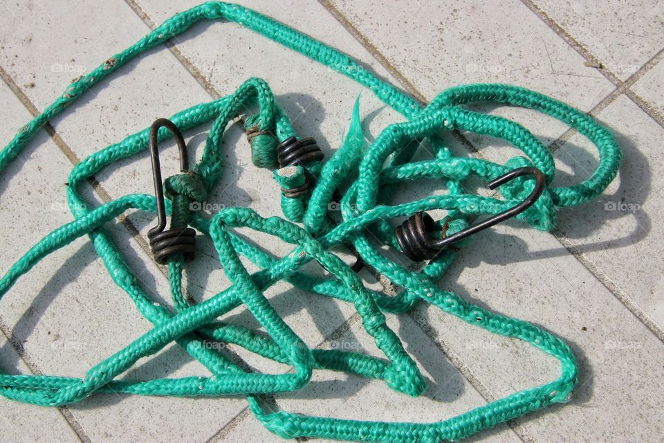 Close-up of a green bungee cord with hook on white table