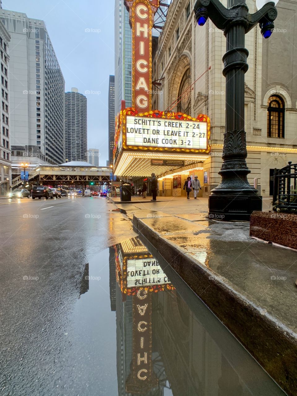 Chicago Theater sign reflecting in a puddle on February 20, 2019. Sign advertising Schitt’s Creek, Lovett or Leave It, and Dane Cook. 