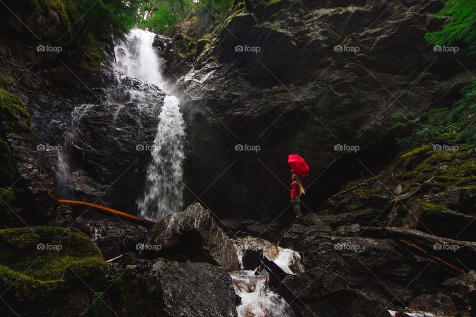 A lady in red suit and umbrella by the beautiful waterfalls.