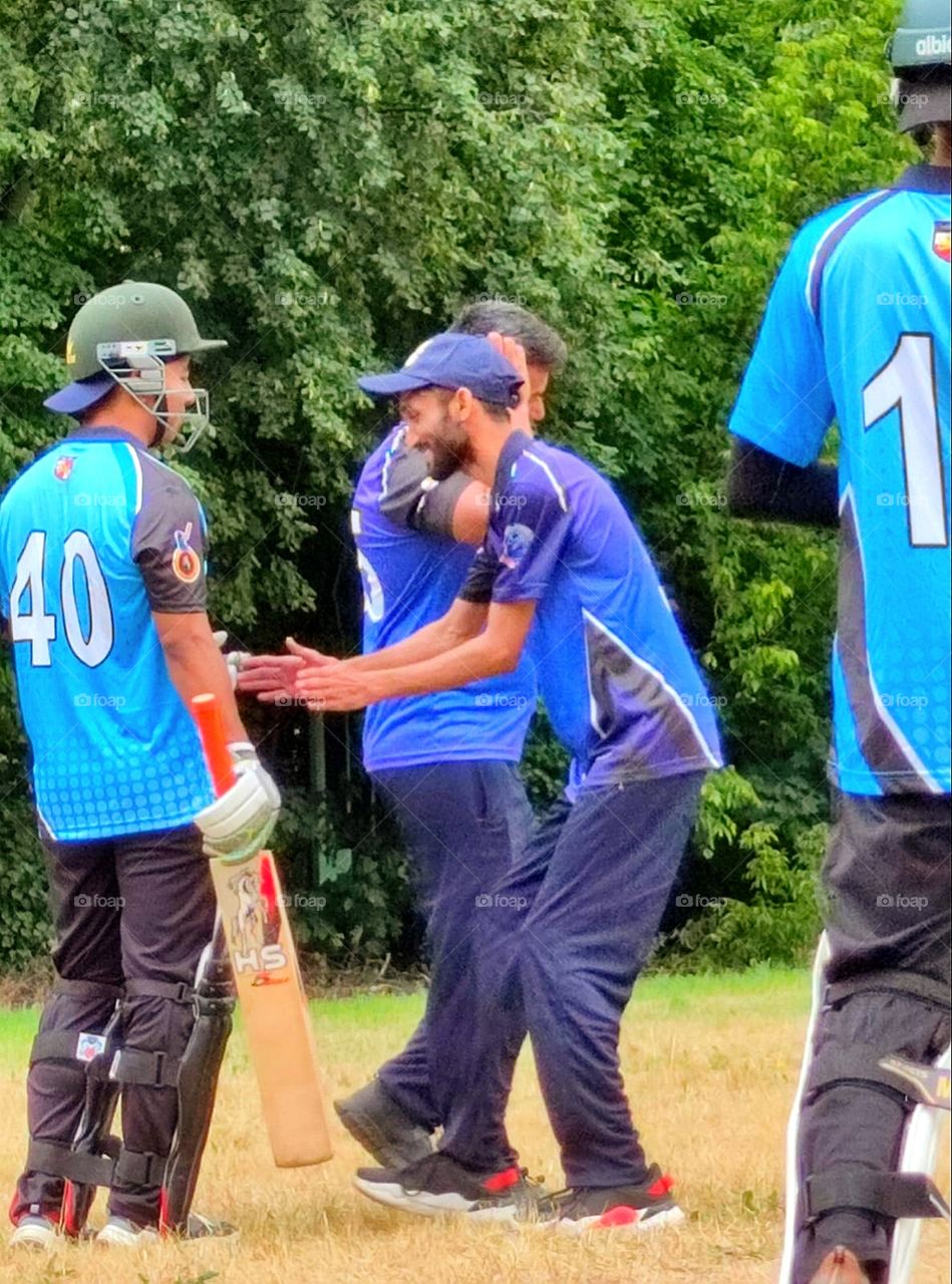 Cricket game.  The players gathered on the field.  One player smiles and dances