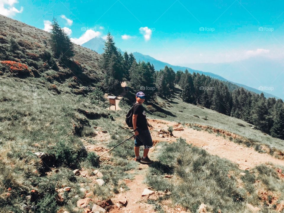 A boy wearing a black backpack is hiking in the mountain