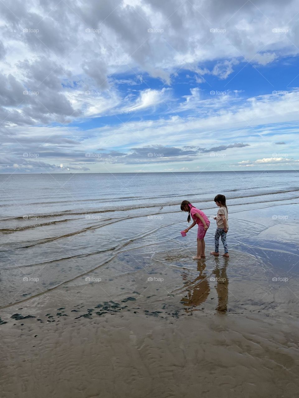  Summer time. Summer day on the beach. Two little girls playing with water.