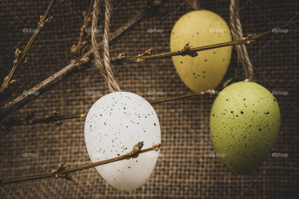 three colorful wooden Easter egg decorations hanging on a branch Infront of a rustic brown background