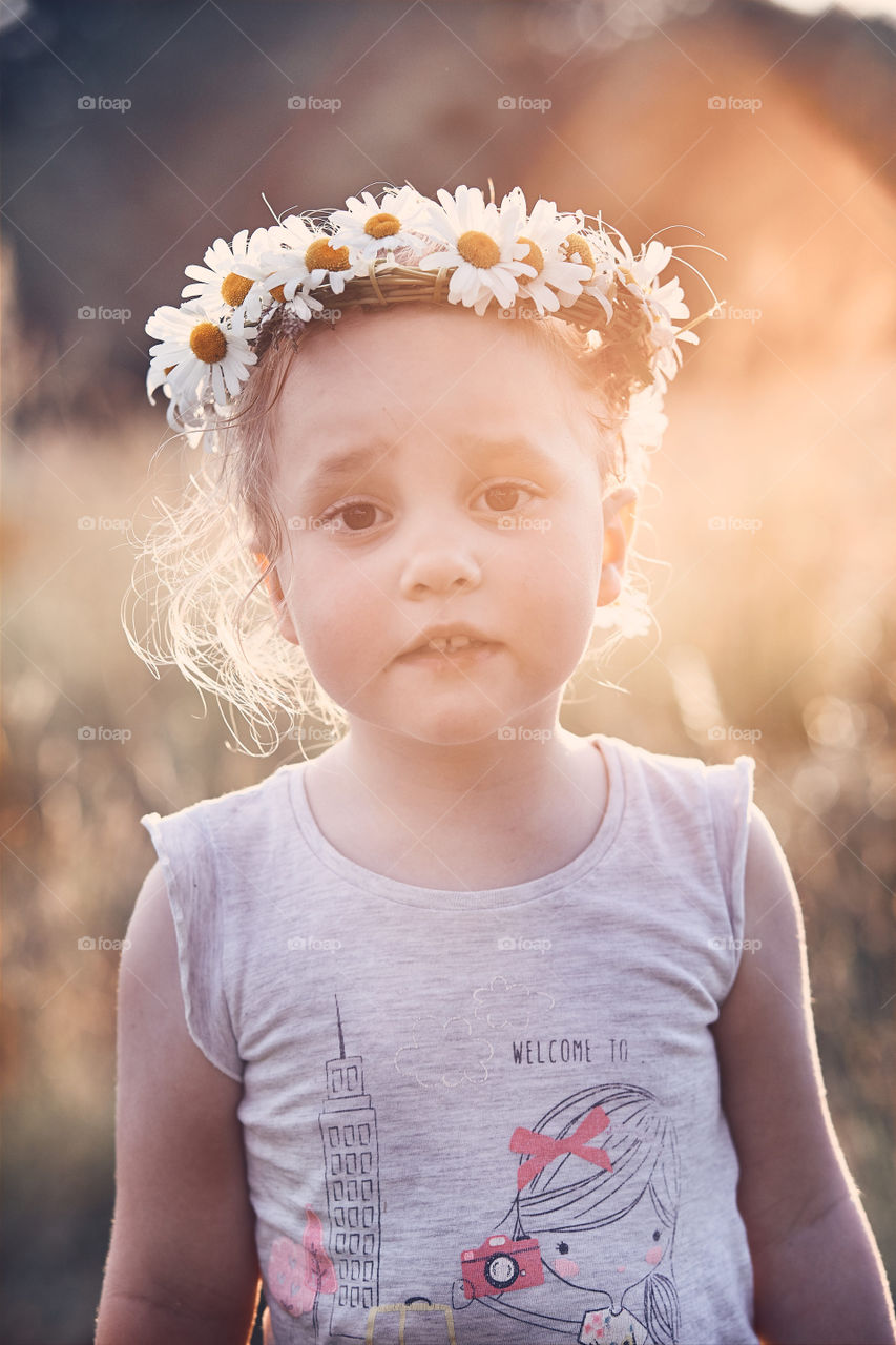 Little girl wearing a coronet of wild flowers on her head. Candid people, real moments, authentic situations