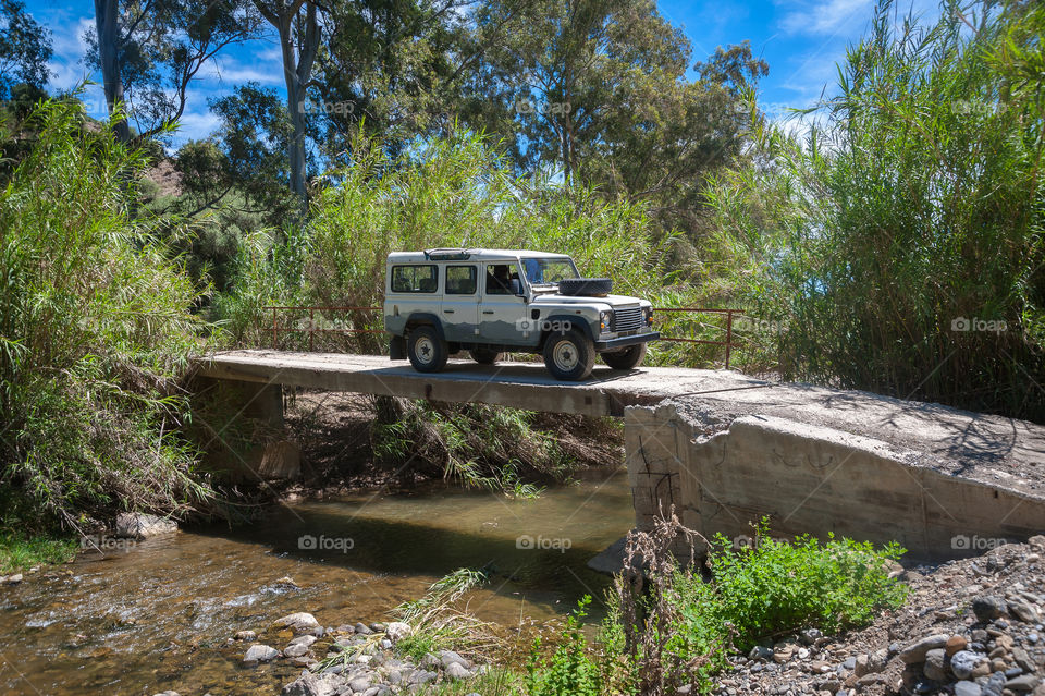 4x4 vehicle crossing stream on derelict crumbling concrete bridge.