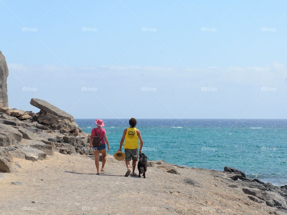 Man and woman dressed in colorful attire walking their dog near the ocean. In Arrecife, Lanzarote.