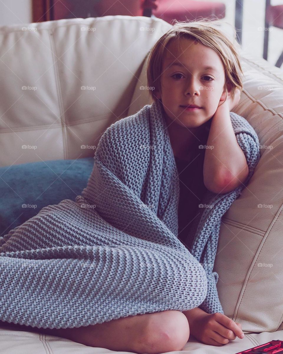 Young boy on sofa wrapped in blanket 